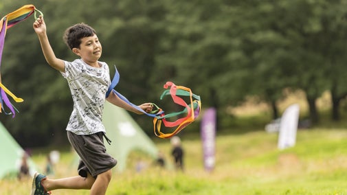 Boy waving around ribbons on the grass.